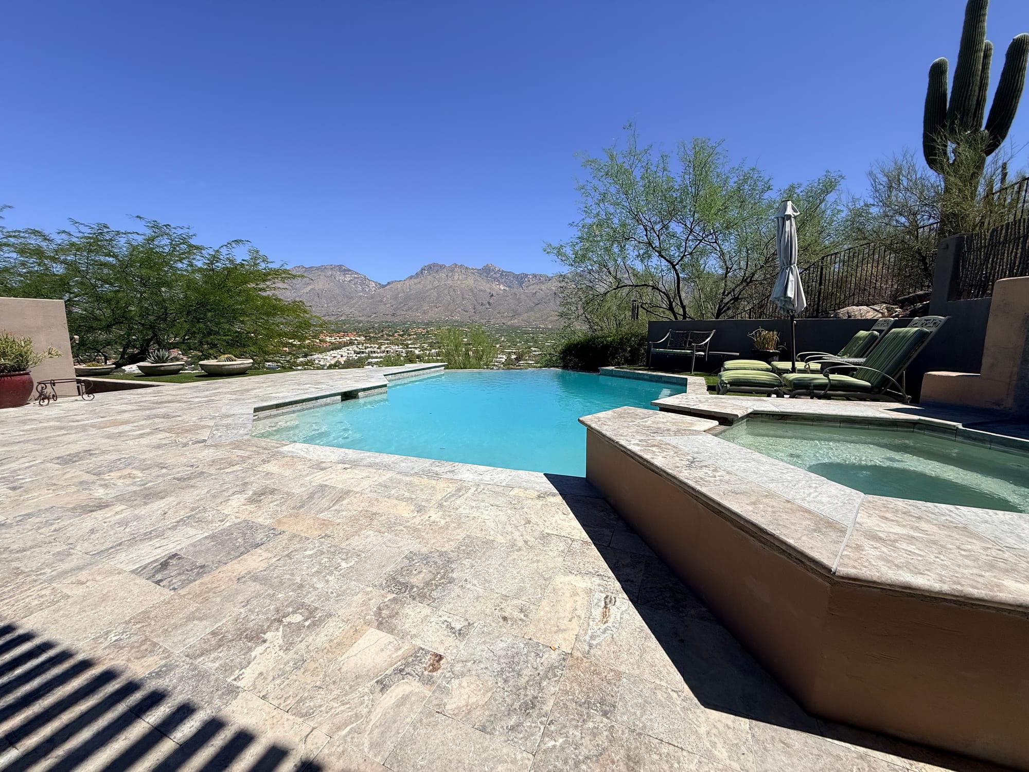 An infinity-edge pool and spa with a travertine deck and mountain view in Tucson by Sorce Signature Outdoors